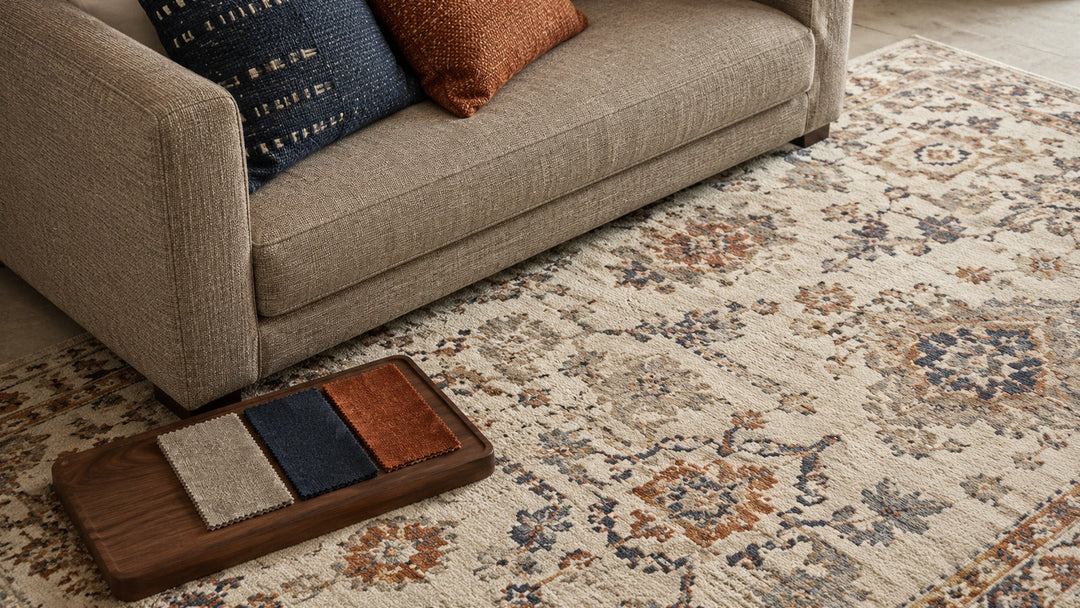 Close view of a greige sofa, Persian-inspired rug and coordinated navy, rust and neutral fabric swatches